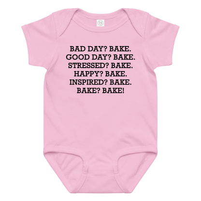 "Bad Day? Bake. Good Day? Bake. Stressed? Bake. Happy? Bake. Inspired? Bake. Bake? Bake!" printed on a pink baby jersey bodysuit laying on a flat surface amongst other clothes