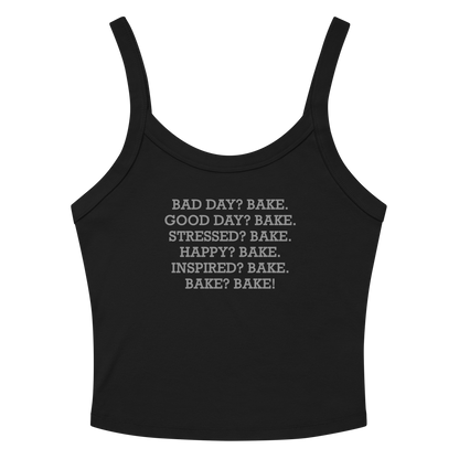 "Bad Day? Bake. Good Day? Bake. Stressed? Bake. Happy? Bake. Inspired? Bake. Bake? Bake!" printed on a solid black blend women's micro-rib tanktop laying on a flat surface amongst sunglasses and shorts
