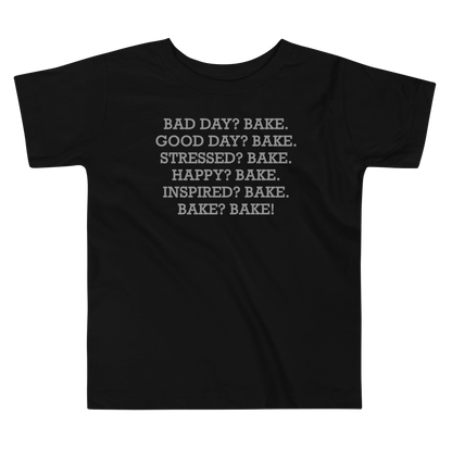 "Bad Day? Bake. Good Day? Bake. Stressed? Bake. Happy? Bake. Inspired? Bake. Bake? Bake!" printed on a black toddler short sleeve tee laying on a flat surface