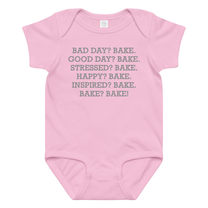"Bad Day? Bake. Good Day? Bake. Stressed? Bake. Happy? Bake. Inspired? Bake. Bake? Bake!" printed on a pink baby jersey bodysuit laying on a flat surface amongst other clothes