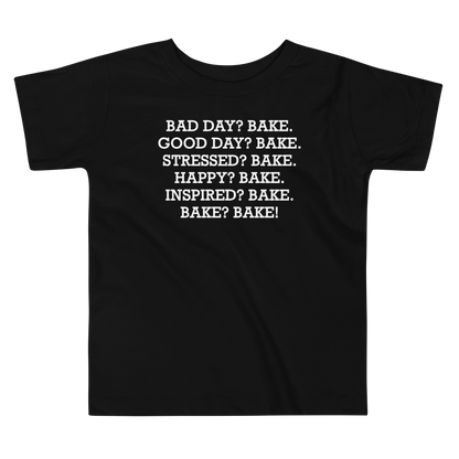 "Bad Day? Bake. Good Day? Bake. Stressed? Bake. Happy? Bake. Inspired? Bake. Bake? Bake!" printed on a black toddler short sleeve tee laying on a flat surface