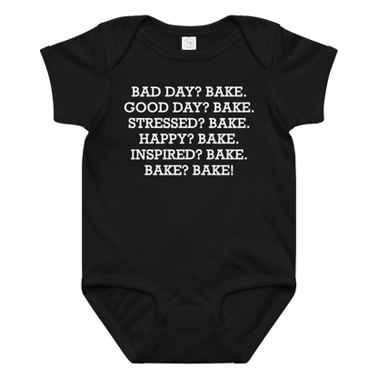 "Bad Day? Bake. Good Day? Bake. Stressed? Bake. Happy? Bake. Inspired? Bake. Bake? Bake!" printed on a black baby jersey bodysuit laying on a flat surface amongst other clothes