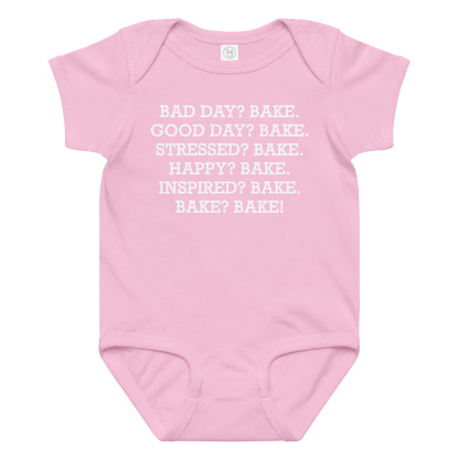"Bad Day? Bake. Good Day? Bake. Stressed? Bake. Happy? Bake. Inspired? Bake. Bake? Bake!" printed on a pink baby jersey bodysuit laying on a flat surface amongst other clothes