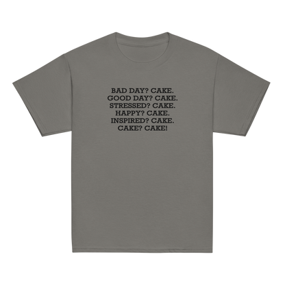 "Bad Day? Cake. Good Day? Cake. Stressed? Cake. Happy? Cake. Inspired? Cake. Cake? Cake!" printed on a charcoal youth classic tee laying on a flat surface