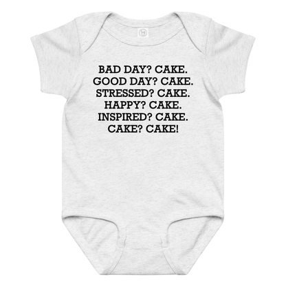 "Bad Day? Cake. Good Day? Cake. Stressed? Cake. Happy? Cake. Inspired? Cake. Cake? Cake!" printed on a ash baby jersey bodysuit laying on a flat surface amongst other clothes