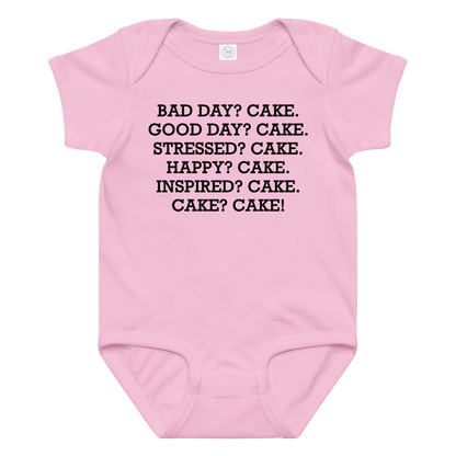 "Bad Day? Cake. Good Day? Cake. Stressed? Cake. Happy? Cake. Inspired? Cake. Cake? Cake!" printed on a pink baby jersey bodysuit laying on a flat surface amongst other clothes