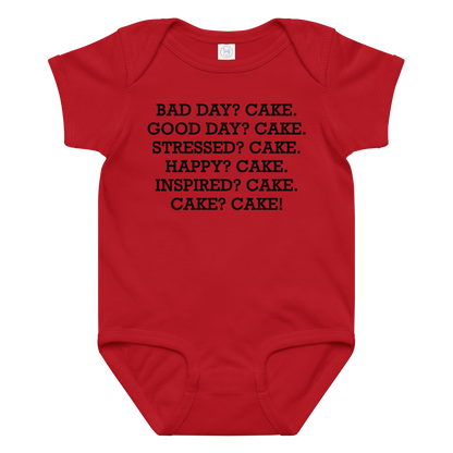 "Bad Day? Cake. Good Day? Cake. Stressed? Cake. Happy? Cake. Inspired? Cake. Cake? Cake!" printed on a red baby jersey bodysuit laying on a flat surface amongst other clothes