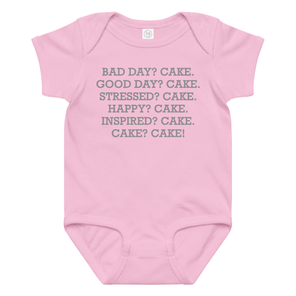 "Bad Day? Cake. Good Day? Cake. Stressed? Cake. Happy? Cake. Inspired? Cake. Cake? Cake!" printed on a pink baby jersey bodysuit laying on a flat surface amongst other clothes