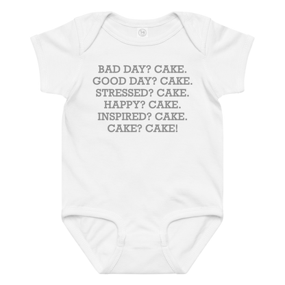 "Bad Day? Cake. Good Day? Cake. Stressed? Cake. Happy? Cake. Inspired? Cake. Cake? Cake!" printed on a white baby jersey bodysuit laying on a flat surface amongst other clothes