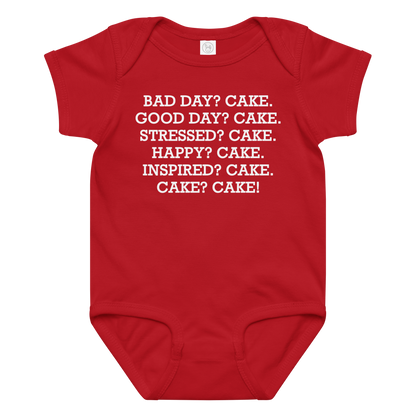 "Bad Day? Cake. Good Day? Cake. Stressed? Cake. Happy? Cake. Inspired? Cake. Cake? Cake!" printed on a red baby jersey bodysuit laying on a flat surface amongst other clothes