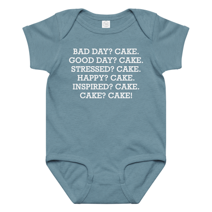 "Bad Day? Cake. Good Day? Cake. Stressed? Cake. Happy? Cake. Inspired? Cake. Cake? Cake!" printed on a vintage indigo baby jersey bodysuit laying on a flat surface amongst other clothes