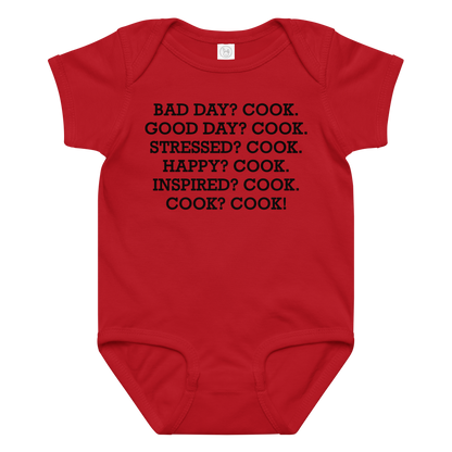 "Bad Day? Cook. Good Day? Cook. Stressed? Cook. Happy? Cook. Inspired? Cook. Cook? Cook!" printed on a red baby jersey bodysuit laying on a flat surface amongst other clothes