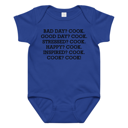"Bad Day? Cook. Good Day? Cook. Stressed? Cook. Happy? Cook. Inspired? Cook. Cook? Cook!" printed on a royal baby jersey bodysuit laying on a flat surface amongst other clothes