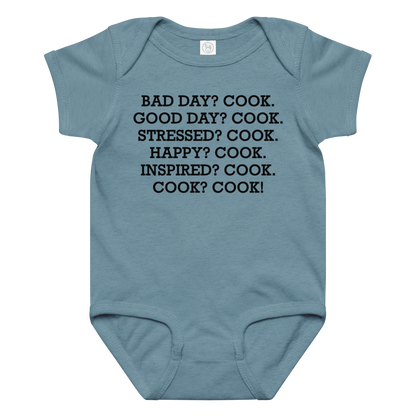 "Bad Day? Cook. Good Day? Cook. Stressed? Cook. Happy? Cook. Inspired? Cook. Cook? Cook!" printed on a vintage indigo baby jersey bodysuit laying on a flat surface amongst other clothes
