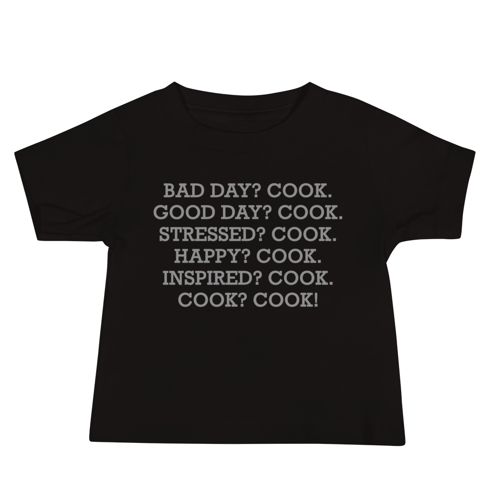 "Bad Day? Cook. Good Day? Cook. Stressed? Cook. Happy? Cook. Inspired? Cook. Cook? Cook!" printed on a black baby jersey short sleeve tee laying on a flat surface