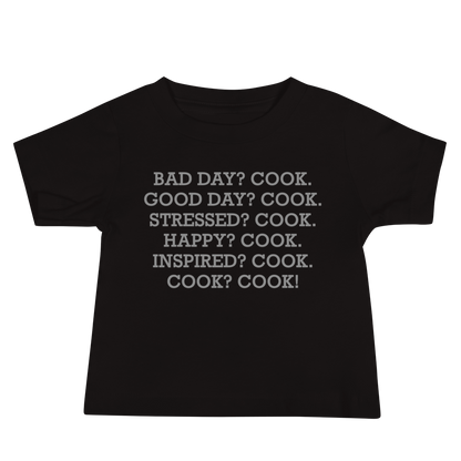 "Bad Day? Cook. Good Day? Cook. Stressed? Cook. Happy? Cook. Inspired? Cook. Cook? Cook!" printed on a black baby jersey short sleeve tee laying on a flat surface