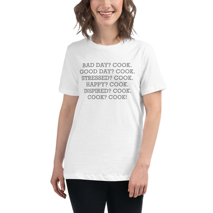 "Bad Day? Cook. Good Day? Cook. Stressed? Cook. Happy? Cook. Inspired? Cook. Cook? Cook!" printed on a white women's relaxed t-shirt worn by a female