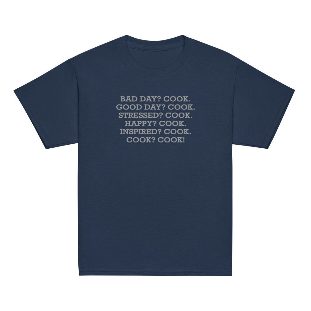 "Bad Day? Cook. Good Day? Cook. Stressed? Cook. Happy? Cook. Inspired? Cook. Cook? Cook!" printed on a navy youth classic tee laying on a flat surface