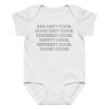 "Bad Day? Cook. Good Day? Cook. Stressed? Cook. Happy? Cook. Inspired? Cook. Cook? Cook!" printed on a ash baby jersey bodysuit laying on a flat surface amongst other clothes