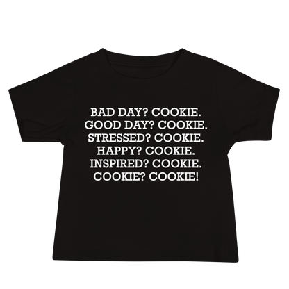 "Bad Day? Cook. Good Day? Cook. Stressed? Cook. Happy? Cook. Inspired? Cook. Cook? Cook!" printed on a black baby jersey short sleeve tee laying on a flat surface