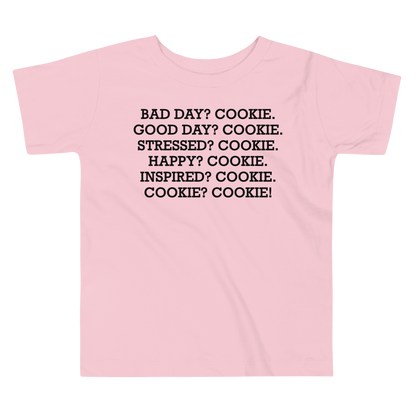 "Bad Day? Cookie. Good Day? Cookie. Stressed? Cookie. Happy? Cookie. Inspired? Cookie. Cookie? Cookie!" printed on a pink toddler short sleeve tee laying on a flat surface