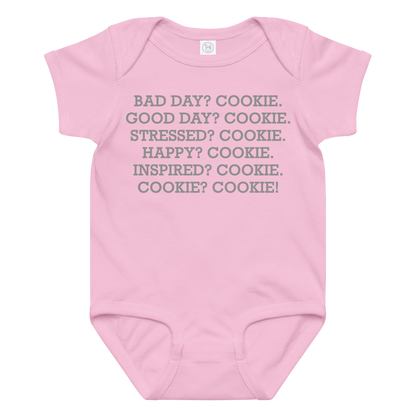 "Bad Day? Cookie. Good Day? Cookie. Stressed? Cookie. Happy? Cookie. Inspired? Cookie. Cookie? Cookie!" printed on a pink baby jersey bodysuit laying on a flat surface amongst other clothes