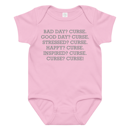 "Bad Day? Curse. Good Day? Curse. Stressed? Curse. Happy? Curse. Inspired? Curse. Curse? Curse!" printed on a pink baby jersey bodysuit laying on a flat surface amongst other clothes