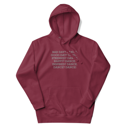 "Bad Day? Dance. Good Day? Dance. Stressed? Dance. Happy? Dance. Inspired? Dance. Dance? Dance!" printed on a maroon unisex hoodie laying on a flat surface with the hood up