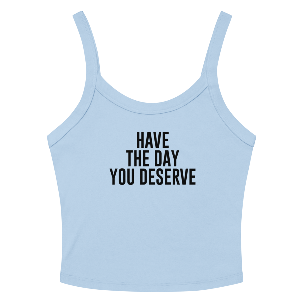 "Have the day you deserve" printed on a solid baby blue blend women's micro-rib tanktop laying on a flat surface amongst sunglasses and shorts