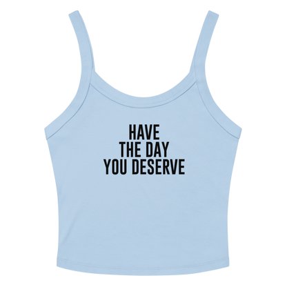 "Have the day you deserve" printed on a solid baby blue blend women's micro-rib tanktop laying on a flat surface amongst sunglasses and shorts