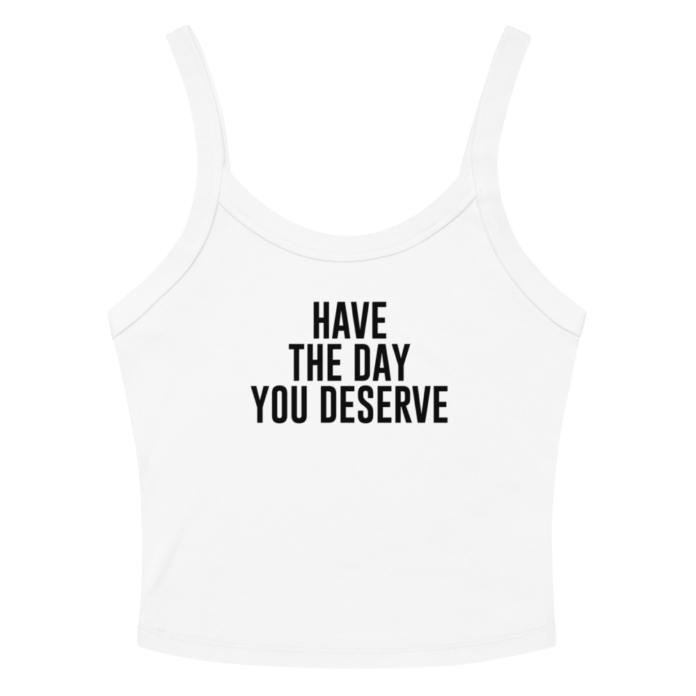 "Have the day you deserve" printed on a solid white blend women's micro-rib tanktop laying on a flat surface amongst sunglasses and shorts