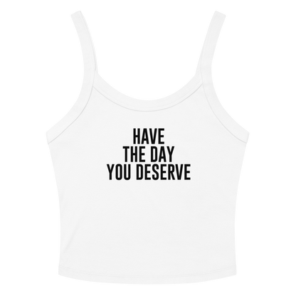 "Have the day you deserve" printed on a solid white blend women's micro-rib tanktop laying on a flat surface amongst sunglasses and shorts