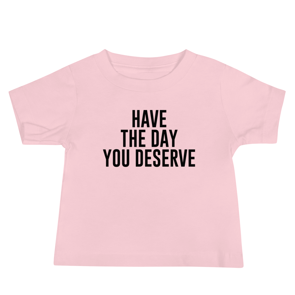 "Have the day you deserve" printed on a pink baby jersey short sleeve tee laying on a flat surface