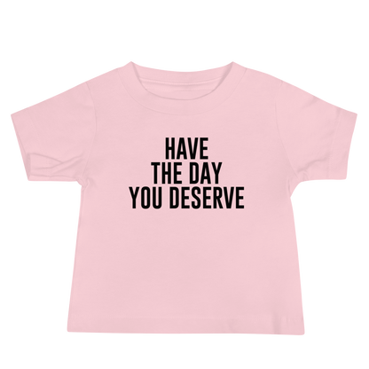 "Have the day you deserve" printed on a pink baby jersey short sleeve tee laying on a flat surface