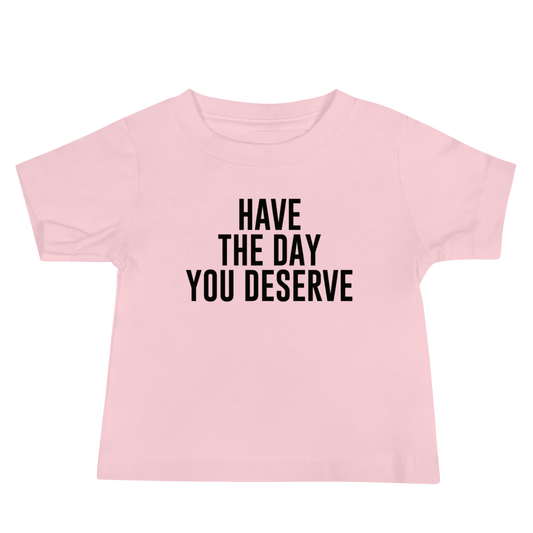 "Have the day you deserve" printed on a pink baby jersey short sleeve tee laying on a flat surface