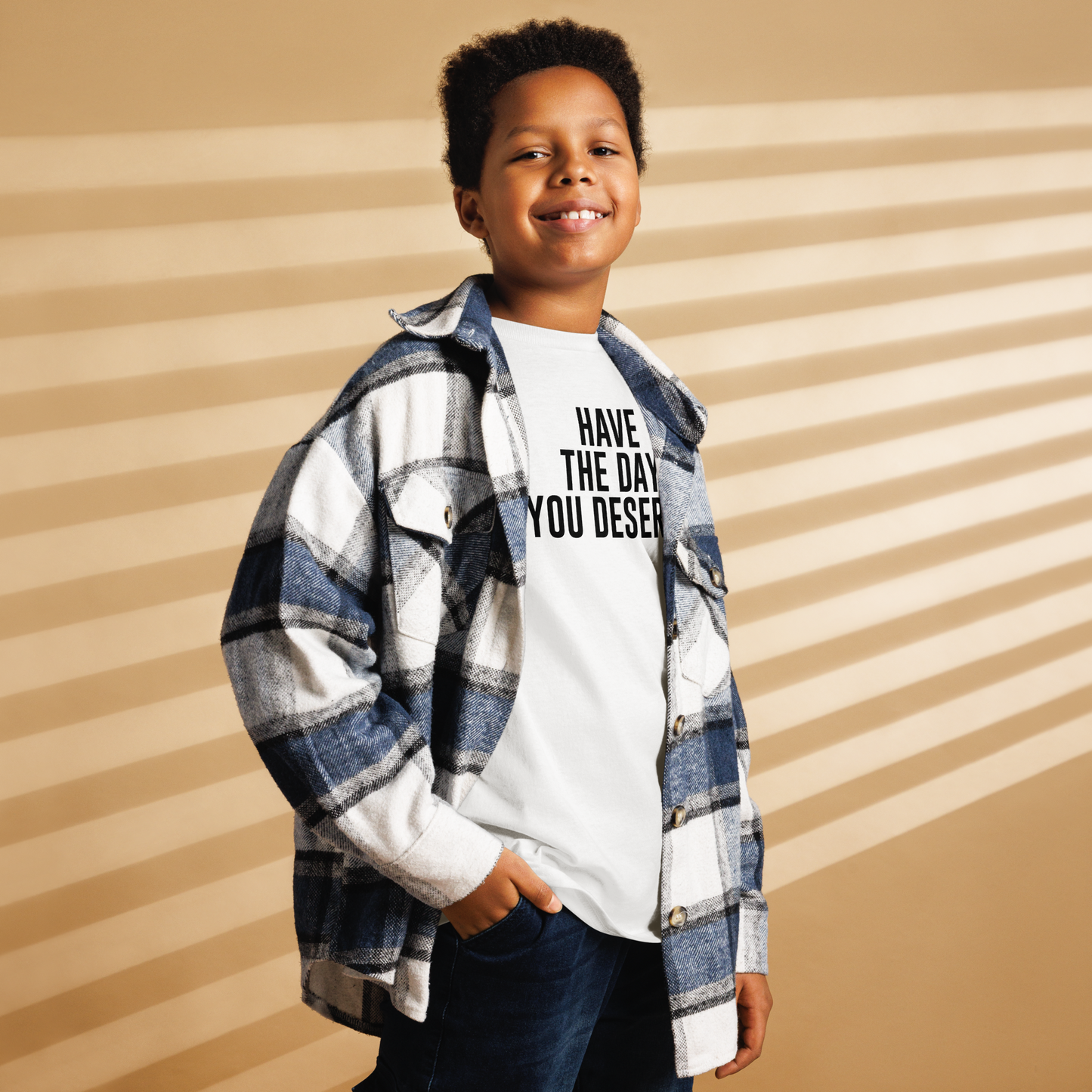 "Have the day you deserve" printed on a white youth classic tee worn by a male also wearing a jacket