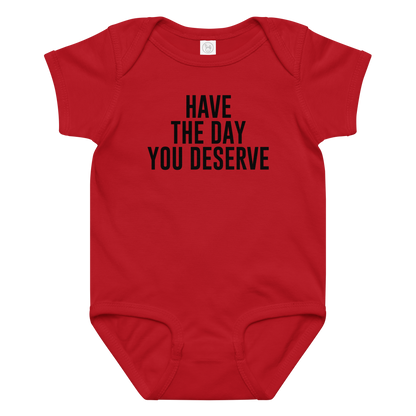 "Have the day you deserve" printed on a red baby jersey bodysuit laying on a flat surface amongst other clothes