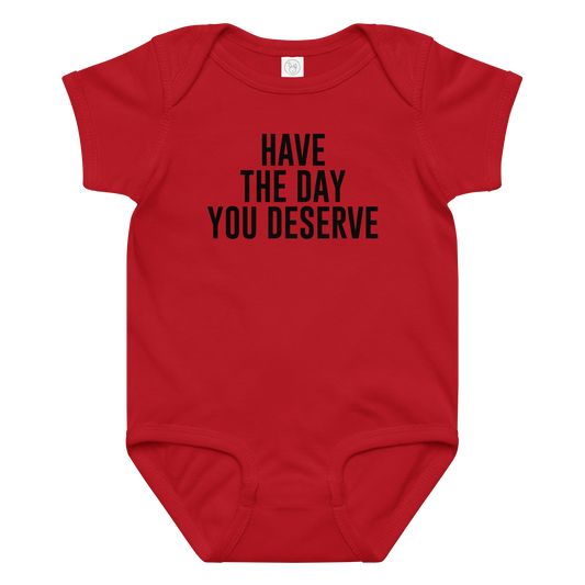"Have the day you deserve" printed on a red baby jersey bodysuit laying on a flat surface amongst other clothes