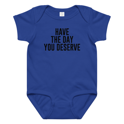 "Have the day you deserve" printed on a royal baby jersey bodysuit laying on a flat surface amongst other clothes