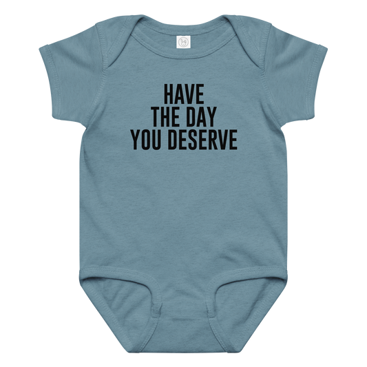 "Have the day you deserve" printed on a vintage indigo baby jersey bodysuit laying on a flat surface amongst other clothes