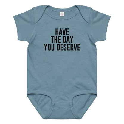 "Have the day you deserve" printed on a vintage indigo baby jersey bodysuit laying on a flat surface amongst other clothes