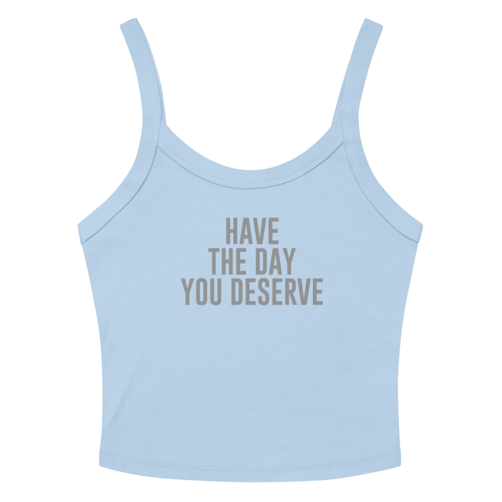 "Have the day you deserve" printed on a solid baby blue blend women's micro-rib tanktop laying on a flat surface amongst sunglasses and shorts