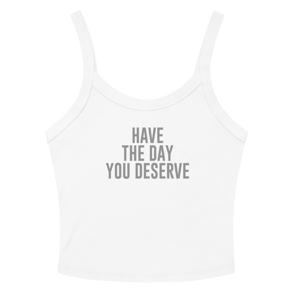 "Have the day you deserve" printed on a solid white blend women's micro-rib tanktop laying on a flat surface amongst sunglasses and shorts