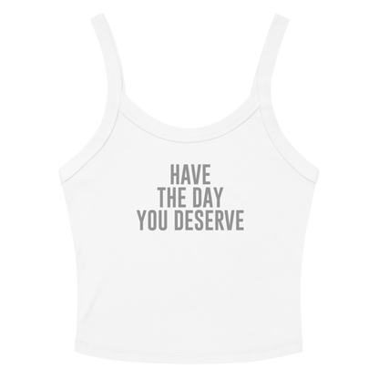 "Have the day you deserve" printed on a solid white blend women's micro-rib tanktop laying on a flat surface amongst sunglasses and shorts