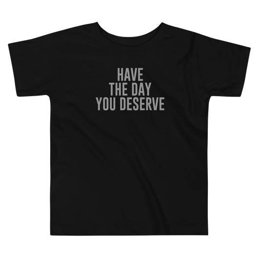 "Have the day you deserve" printed on a black toddler short sleeve tee laying on a flat surface