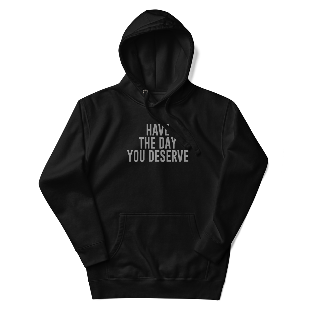 "Have the day you deserve" printed on a black unisex hoodie laying on a flat surface with the hood up