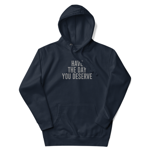 "Have the day you deserve" printed on a navy blazer unisex hoodie laying on a flat surface with the hood up