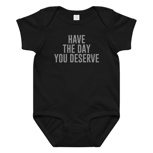 "Have the day you deserve" printed on a black baby jersey bodysuit laying on a flat surface amongst other clothes