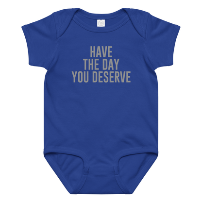 "Have the day you deserve" printed on a royal baby jersey bodysuit laying on a flat surface amongst other clothes