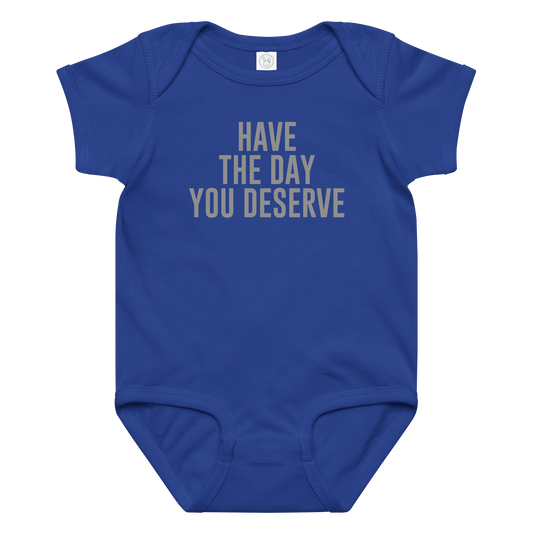 "Have the day you deserve" printed on a royal baby jersey bodysuit laying on a flat surface amongst other clothes